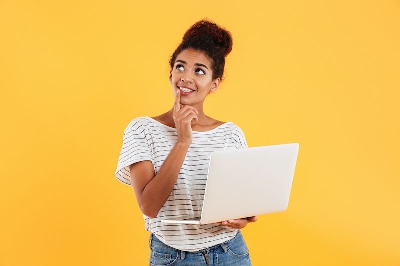 Woman holding laptop and thinking on yellow background