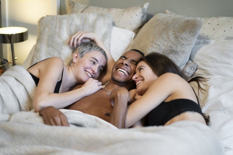 Three people in bed together smiling