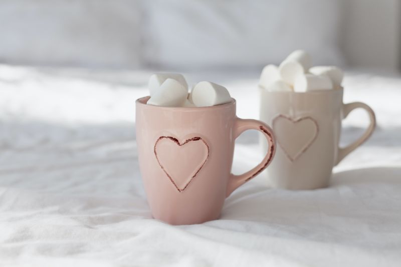 Two mugs of hot chocolate with marshmallows in bed