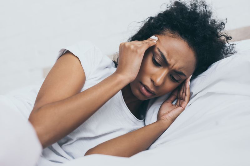 Upset woman holding temples in bed