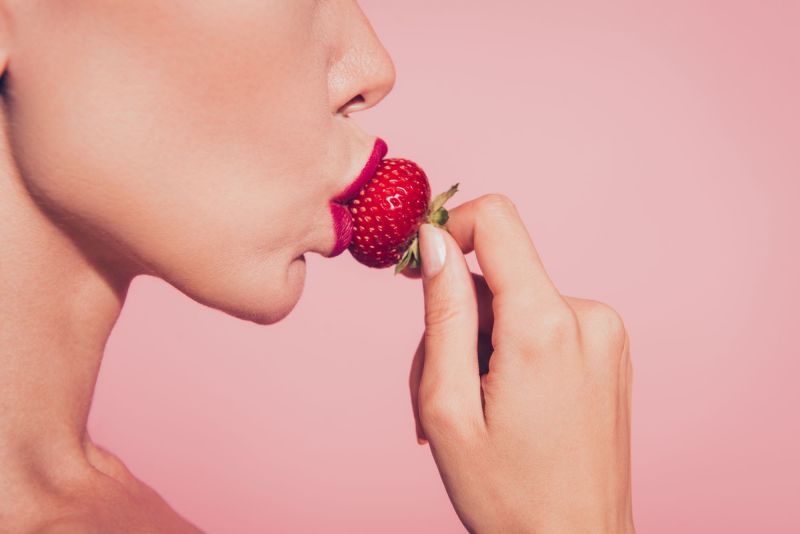 Woman eating strawberry on pink background