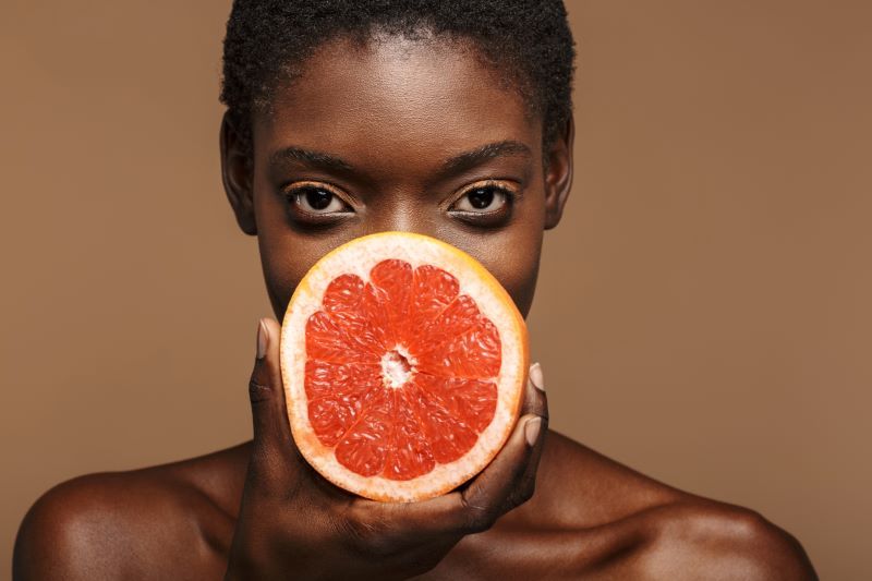 Woman holding half a grapefruit on brown background