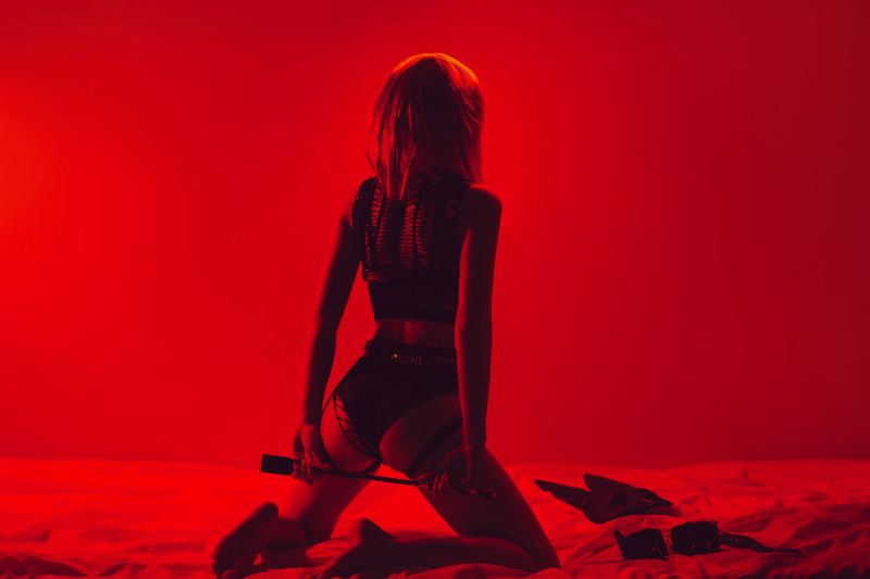 Femme en tenue BDSM tenant un fouet à genoux sur le lit
