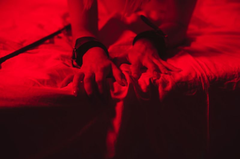 Woman's hand in BDSM cuffs under red lighting