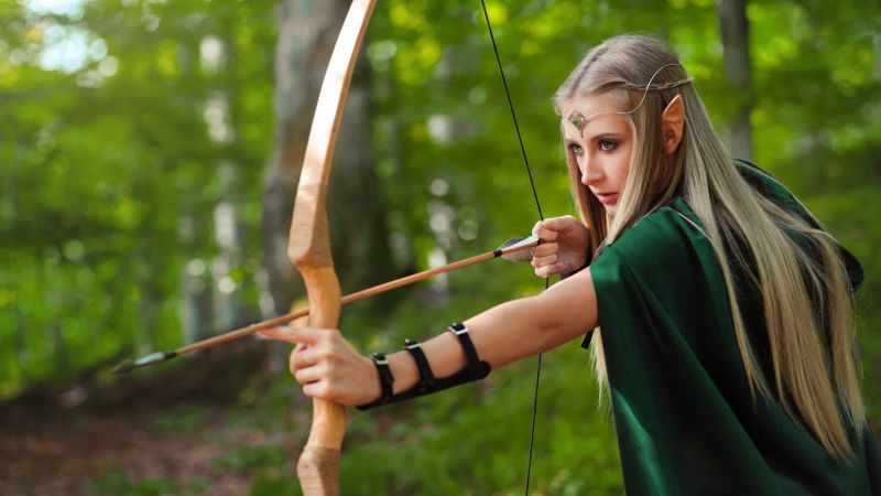 Cosplay woman holding bow and arrow in forest