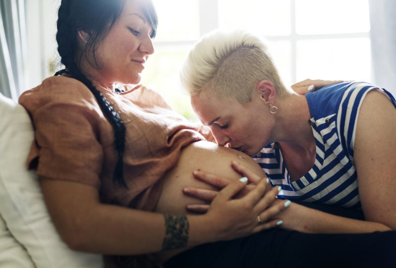 Woman kisses stomach of pregnant girlfriend