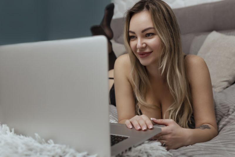 Femme allongée sur le lit sur un ordinateur portable en lingerie