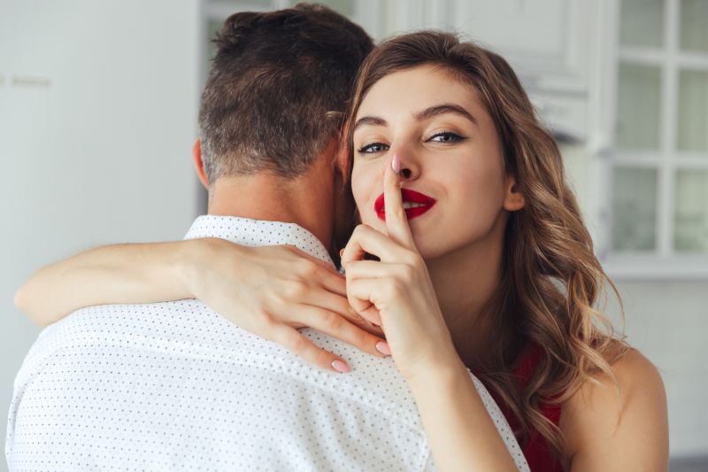 Woman making silence gesture while hugging man