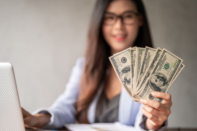 Woman on laptop holding cash