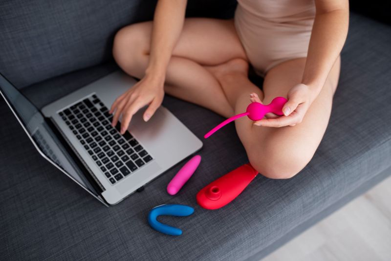 Woman on sofa on laptop with sex toys