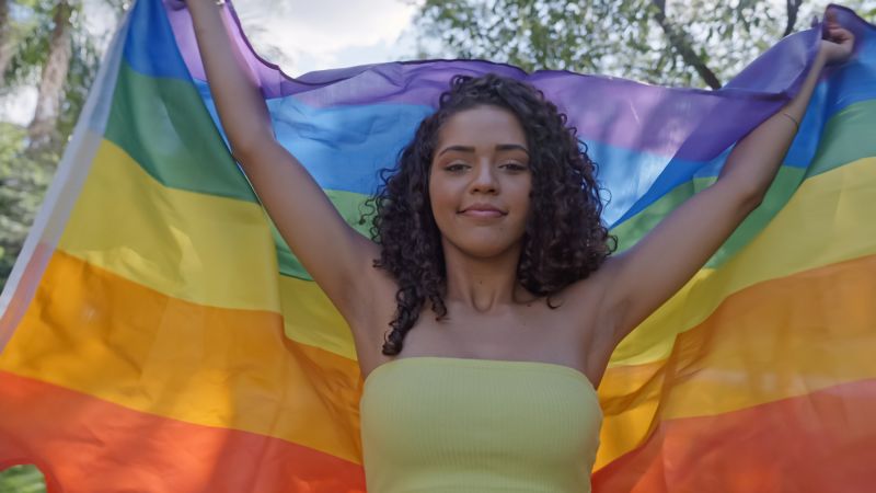 Femme posant avec un drapeau LGBTQ+ à l'extérieur