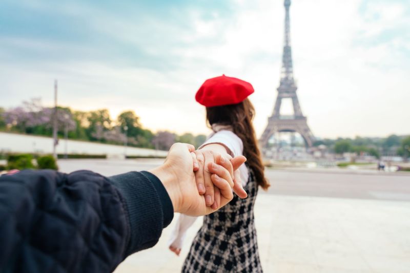Woman pulling man's hands in front of Eiffel Tower
