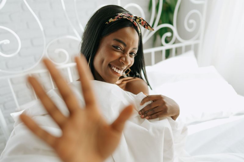 Woman smiling and showing hand at home in bed