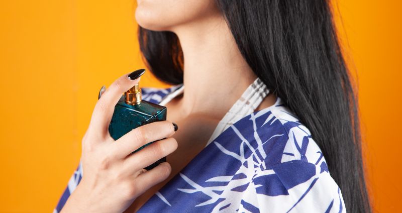 Woman spraying perfume on neck with yellow background