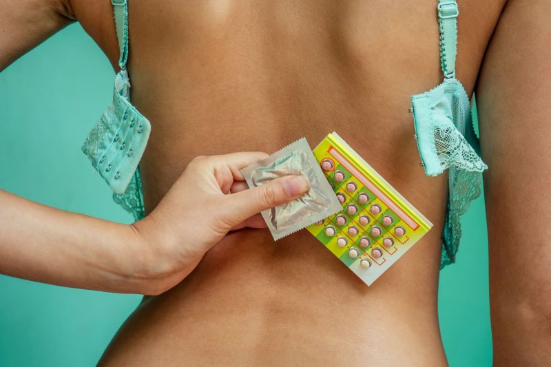 Woman with undone bra holding condom and pill