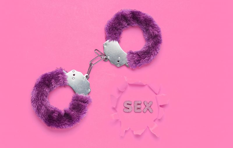 Word sex next to purple handcuffs on pink background