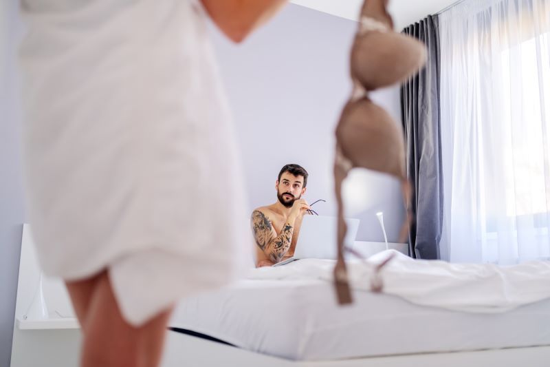 Young tattooed man in bed with girlfriend holding her bra