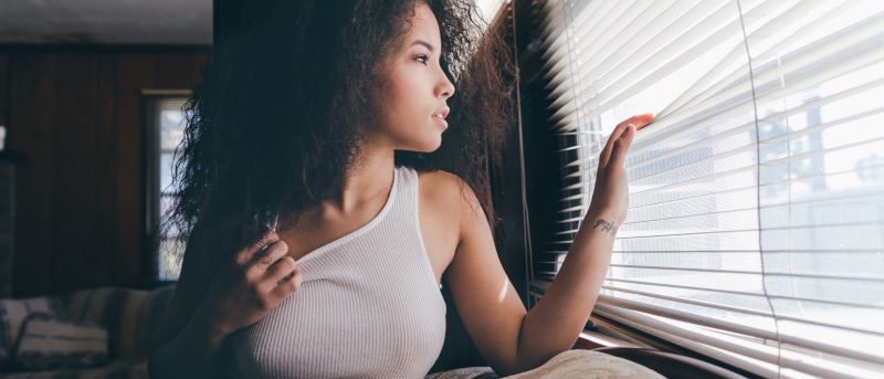 Femme lorgnant à travers les stores à la maison