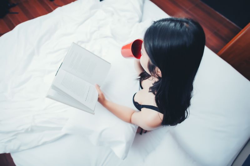 Woman reading and drinking from a mug in bed