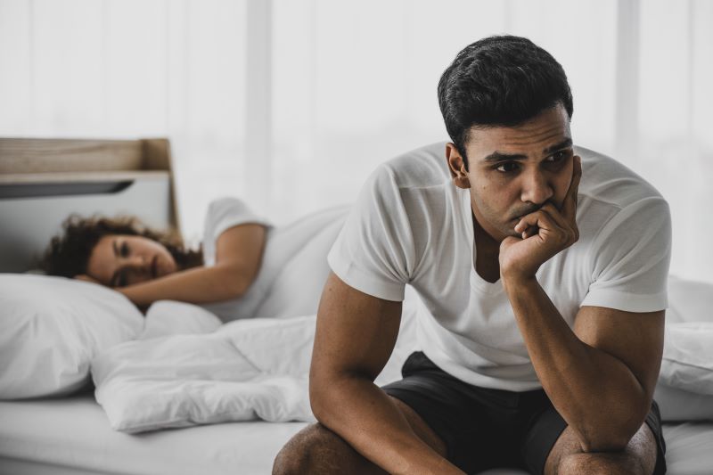 Worried man sat next to partner in bed