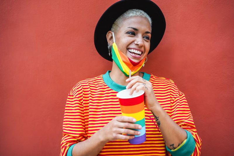 Young smiling woman holding drink with rainbow mask