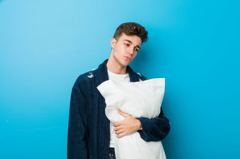Young tired man holding a pillow